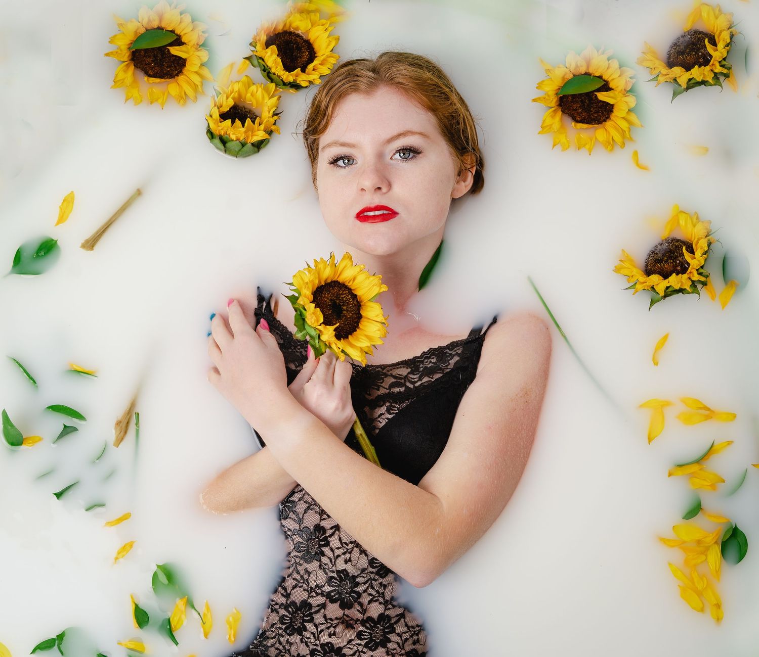 Artistic portrait with scattered sunflowers on white background wearing black lace dress.
