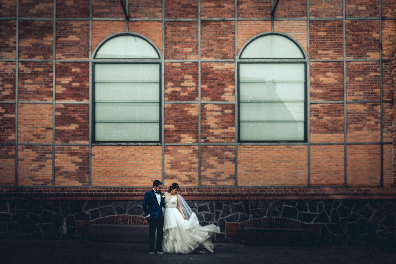 Couple standing in front of brick building with arched windows for elegant wedding portraits.