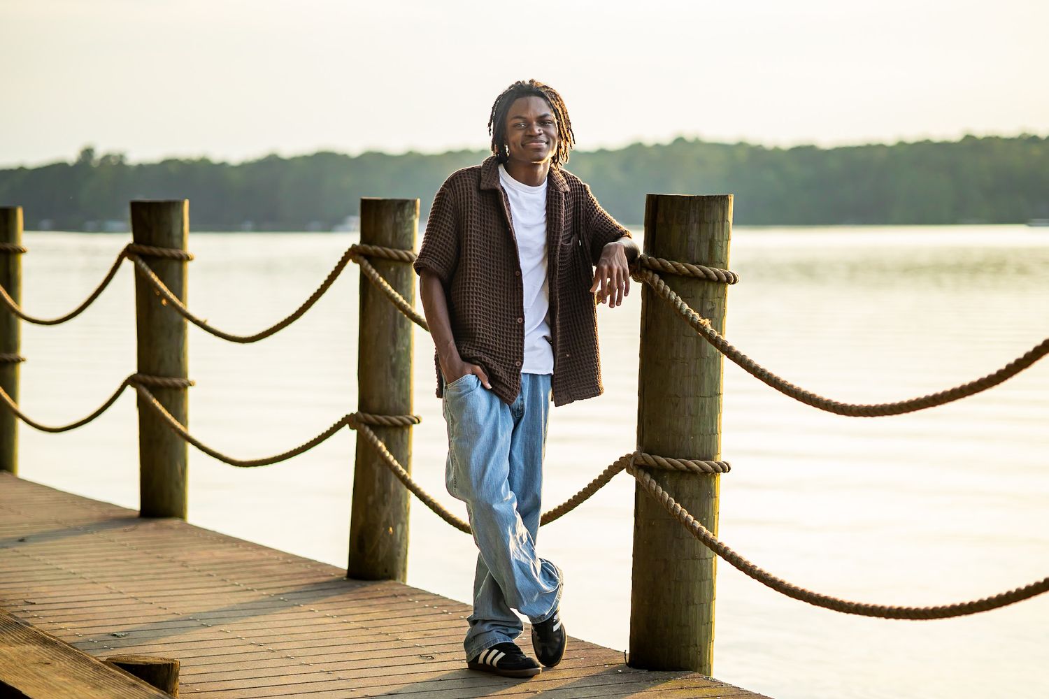 Person standing on wooden dock with rope railing at sunset.