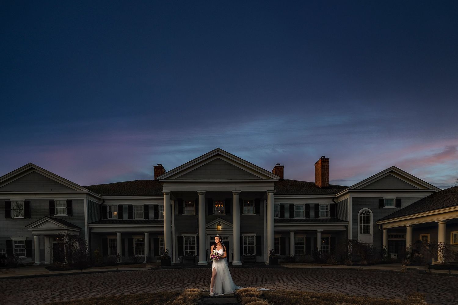 A dramatic twilight wedding photo in front of a grand colonial mansion with white columns.