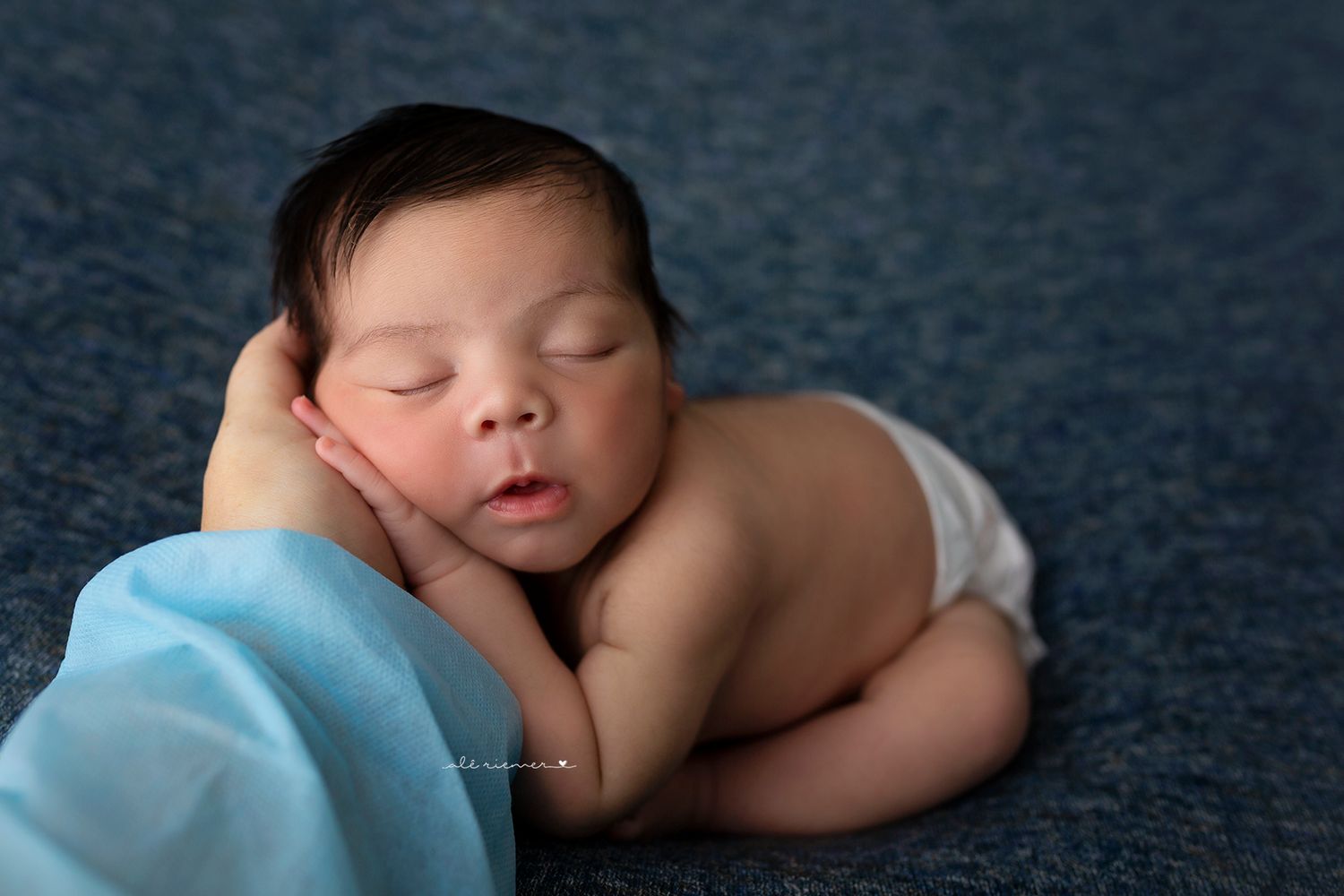 Sleeping newborn in white diaper on blue blanket.