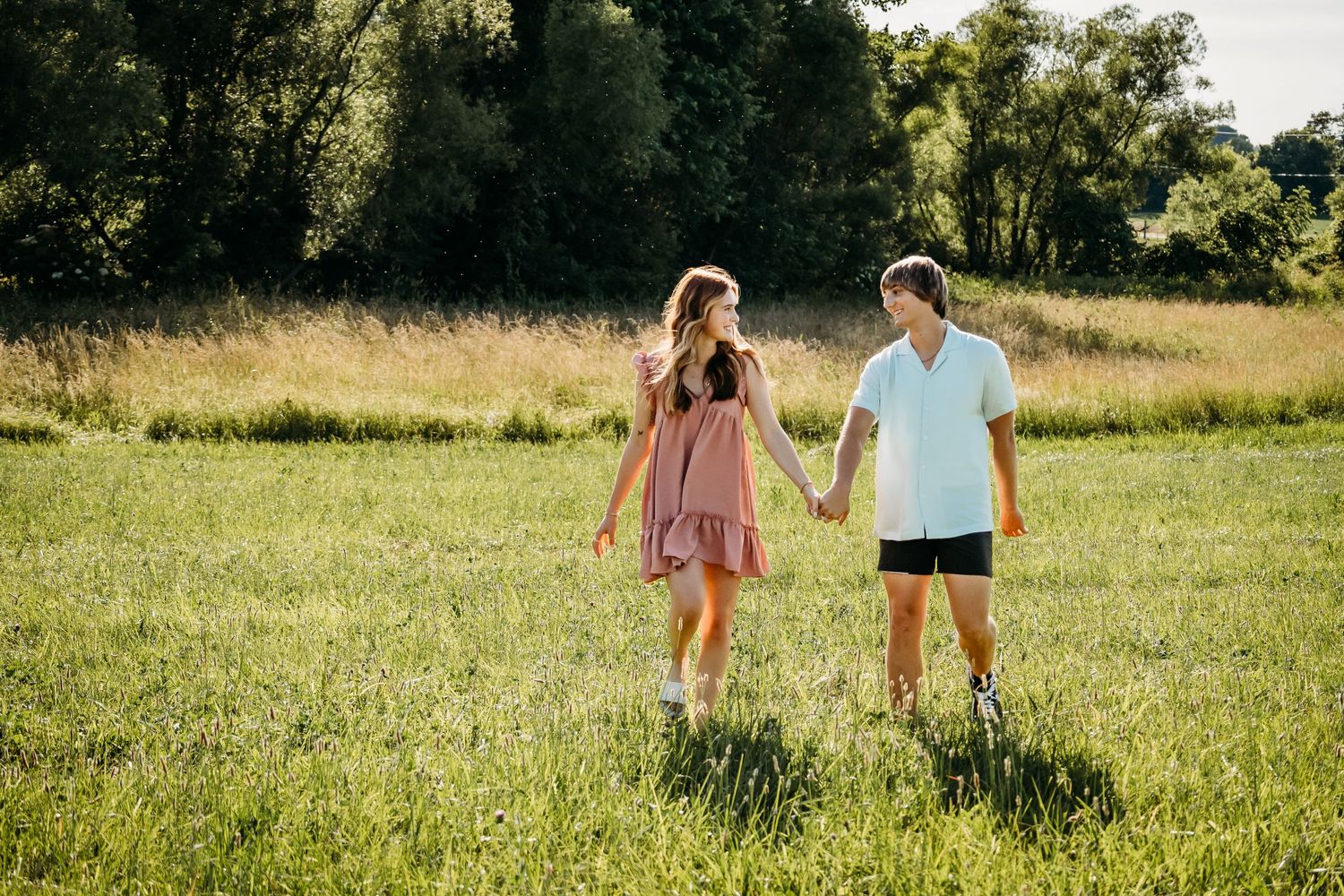 couple holding hands and walking through field during photo session