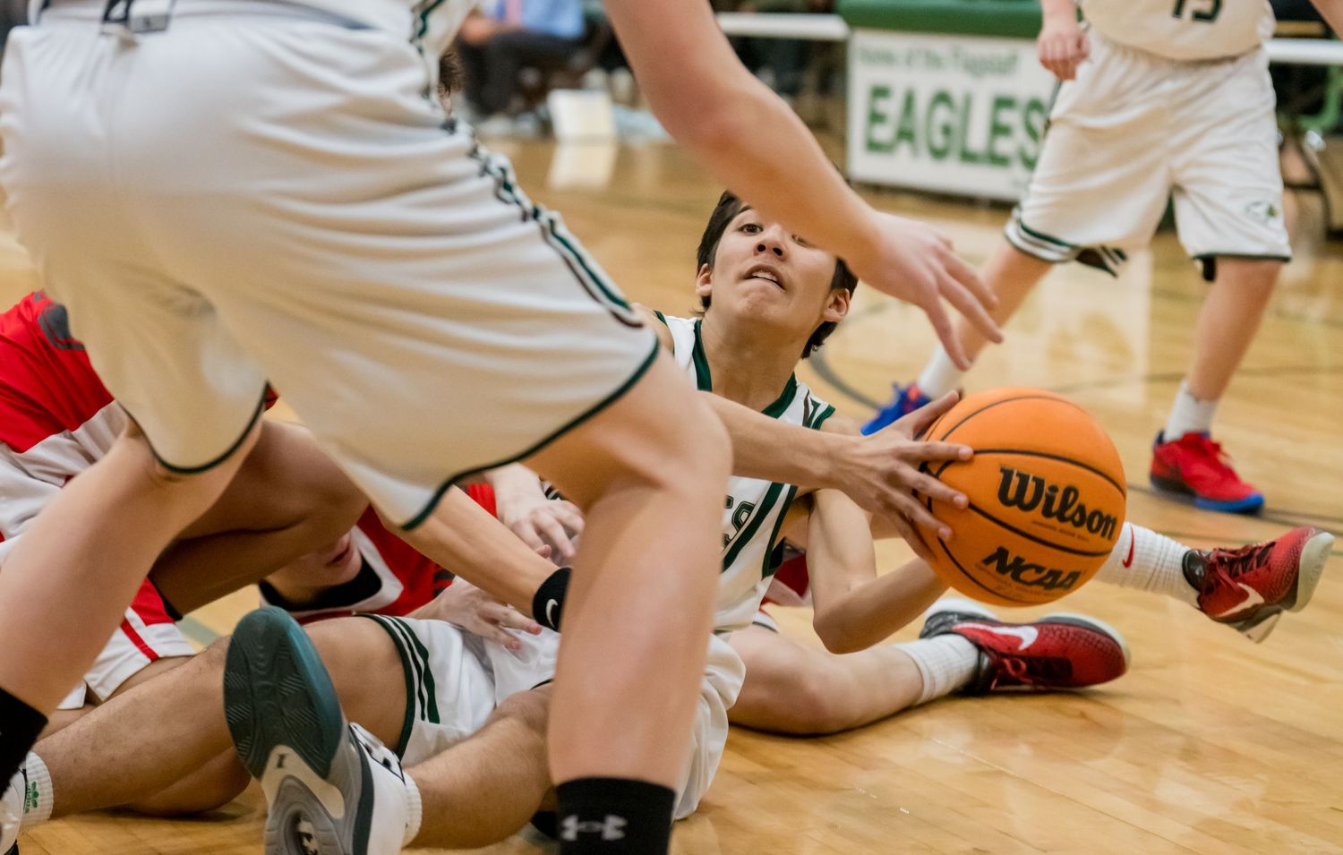 Intense basketball action as players scramble for loose ball on hardwood court.