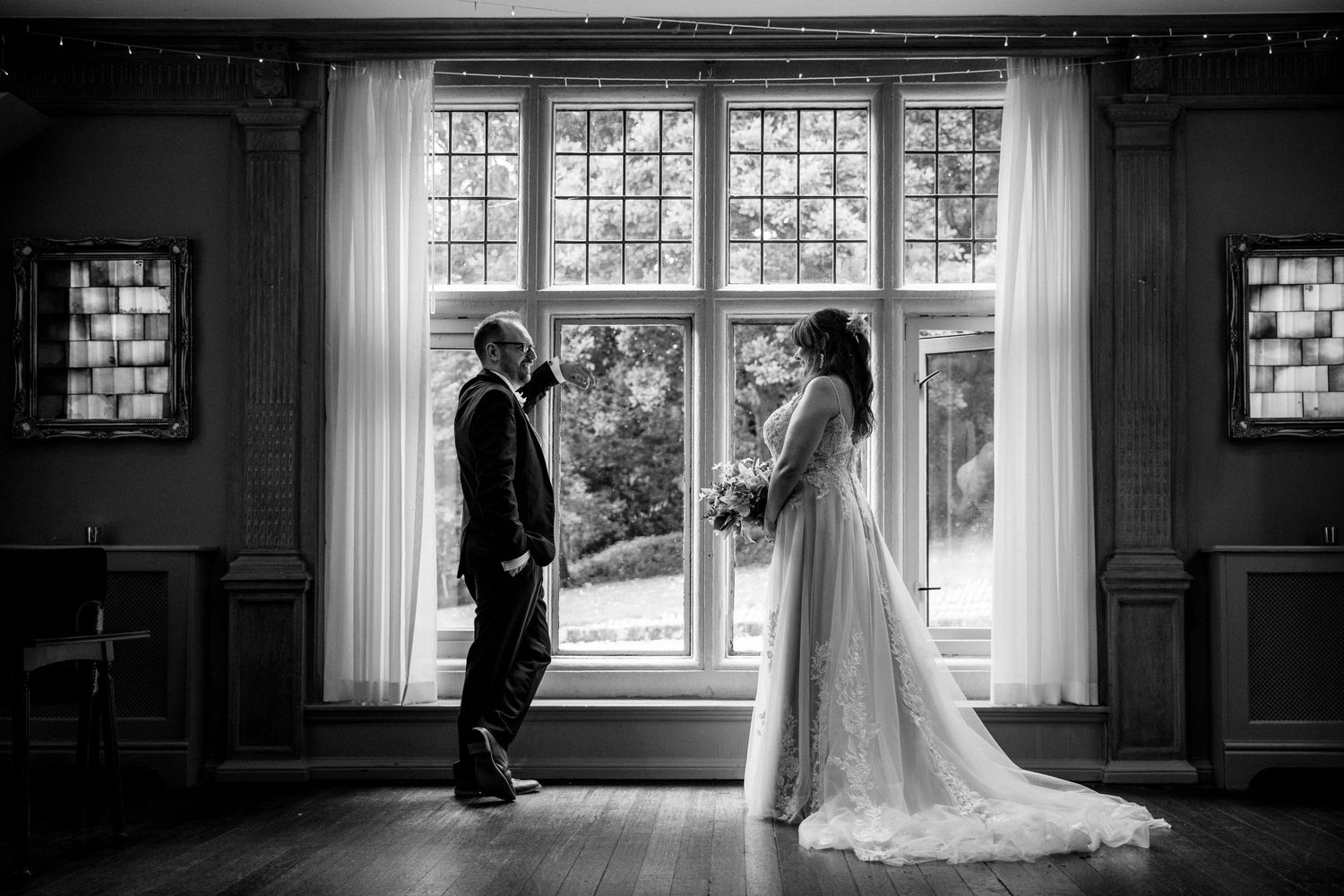 Black and white wedding photos showing couple by large windows in dramatic lighting.