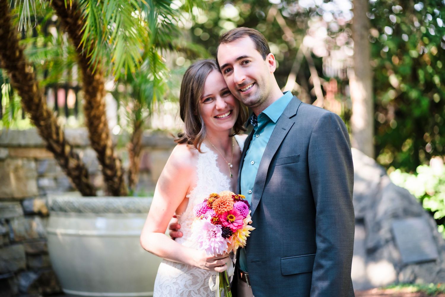 Wedding couple poses with pink bouquet in garden setting with natural greenery.