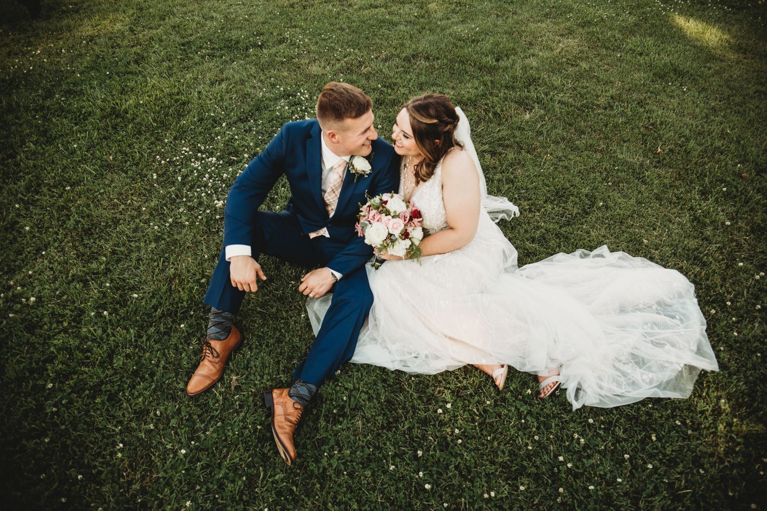 Wedding couple lounging on grass surrounded by delicate white wildflowers.