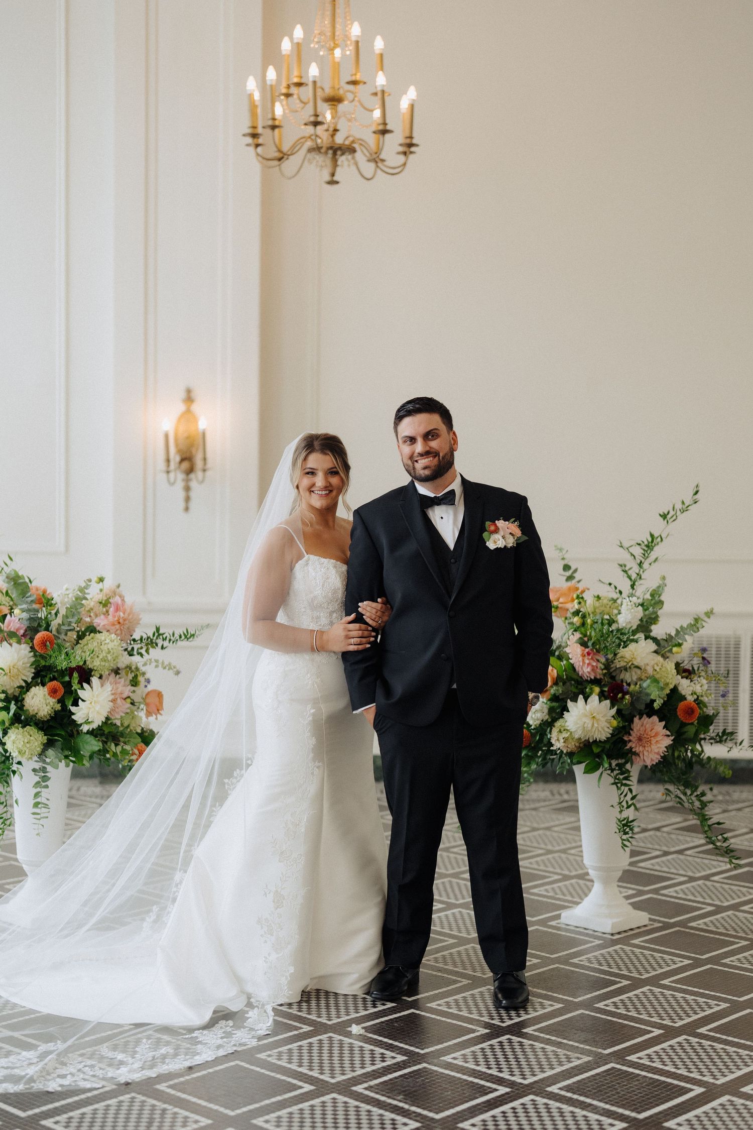 Newlyweds share intimate moment in elegant venue with chandelier and floral decorations.