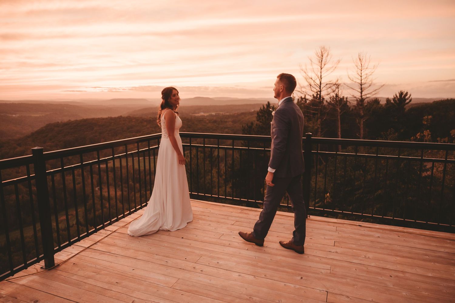 A couple shares a moment on a scenic deck overlooking a sunset mountain landscape.
