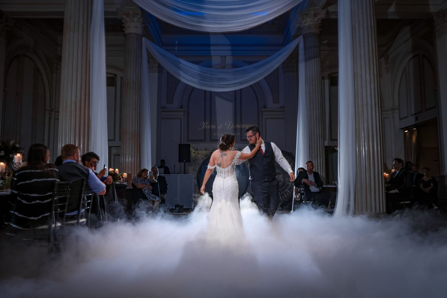 Dramatic wedding dance on fog-covered floor under blue draped ceiling.