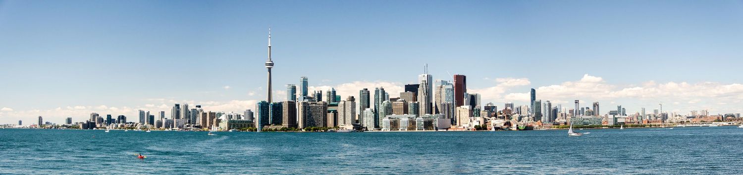 Panoramic skyline view of Toronto's downtown waterfront with CN Tower and modern buildings reflected in Lake Ontario.