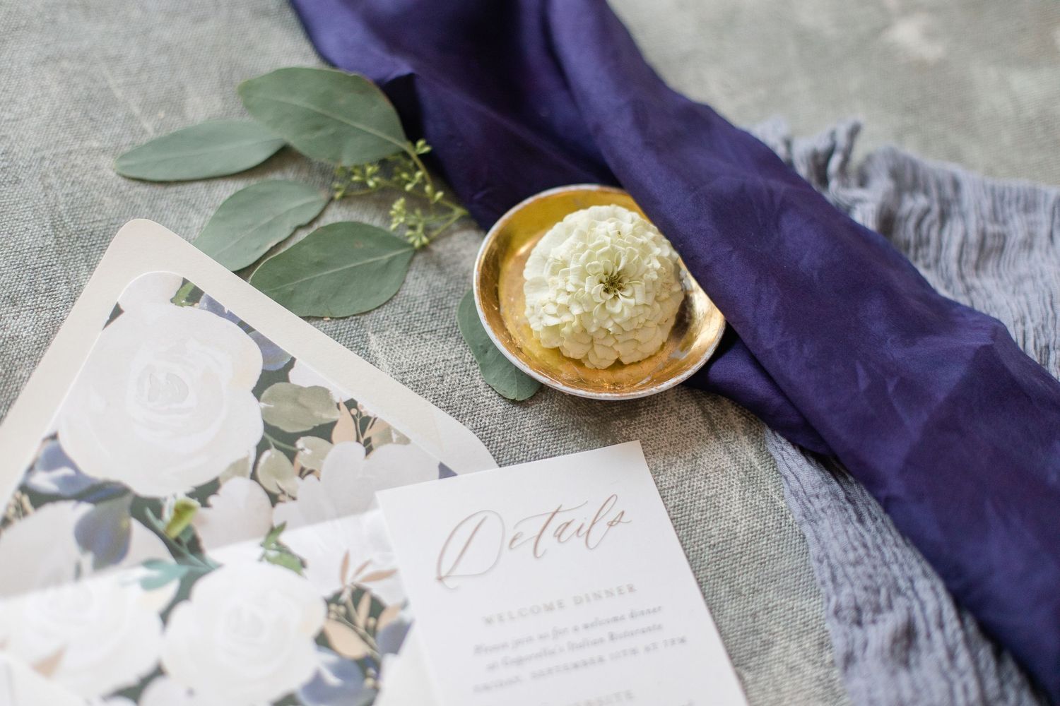 Wedding stationery with purple fabric and greenery flat lay styling.