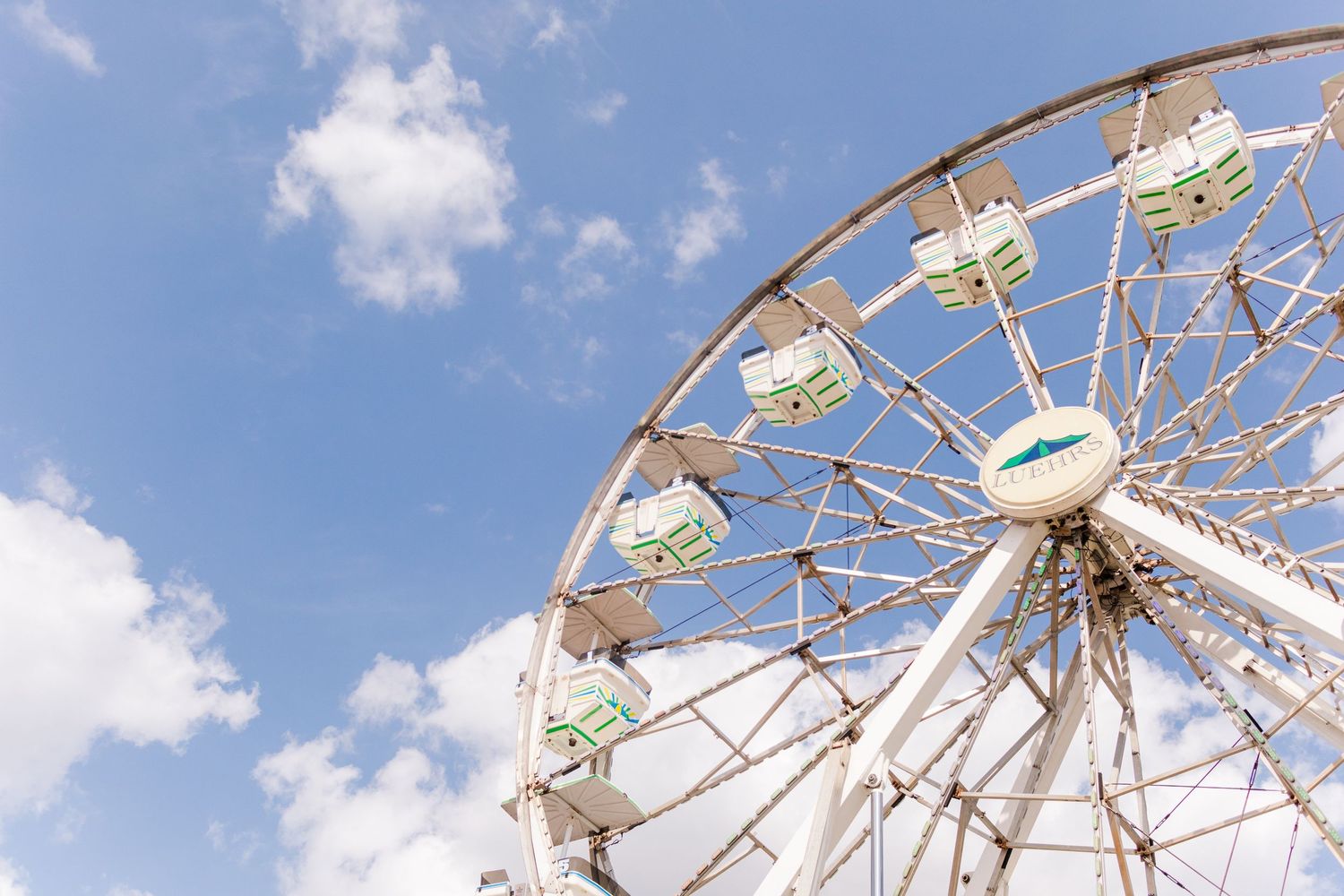 Classic white Ferris wheel against a bright blue sky with puffy clouds.