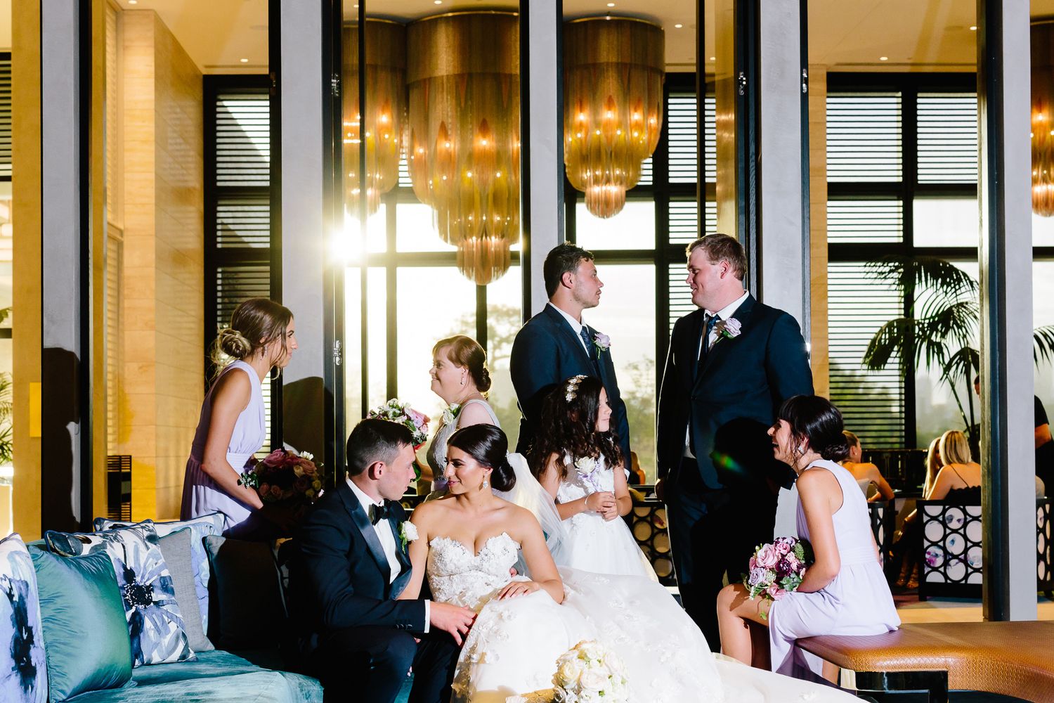 Wedding party lounges in an elegant room with chandeliers and high ceilings.
