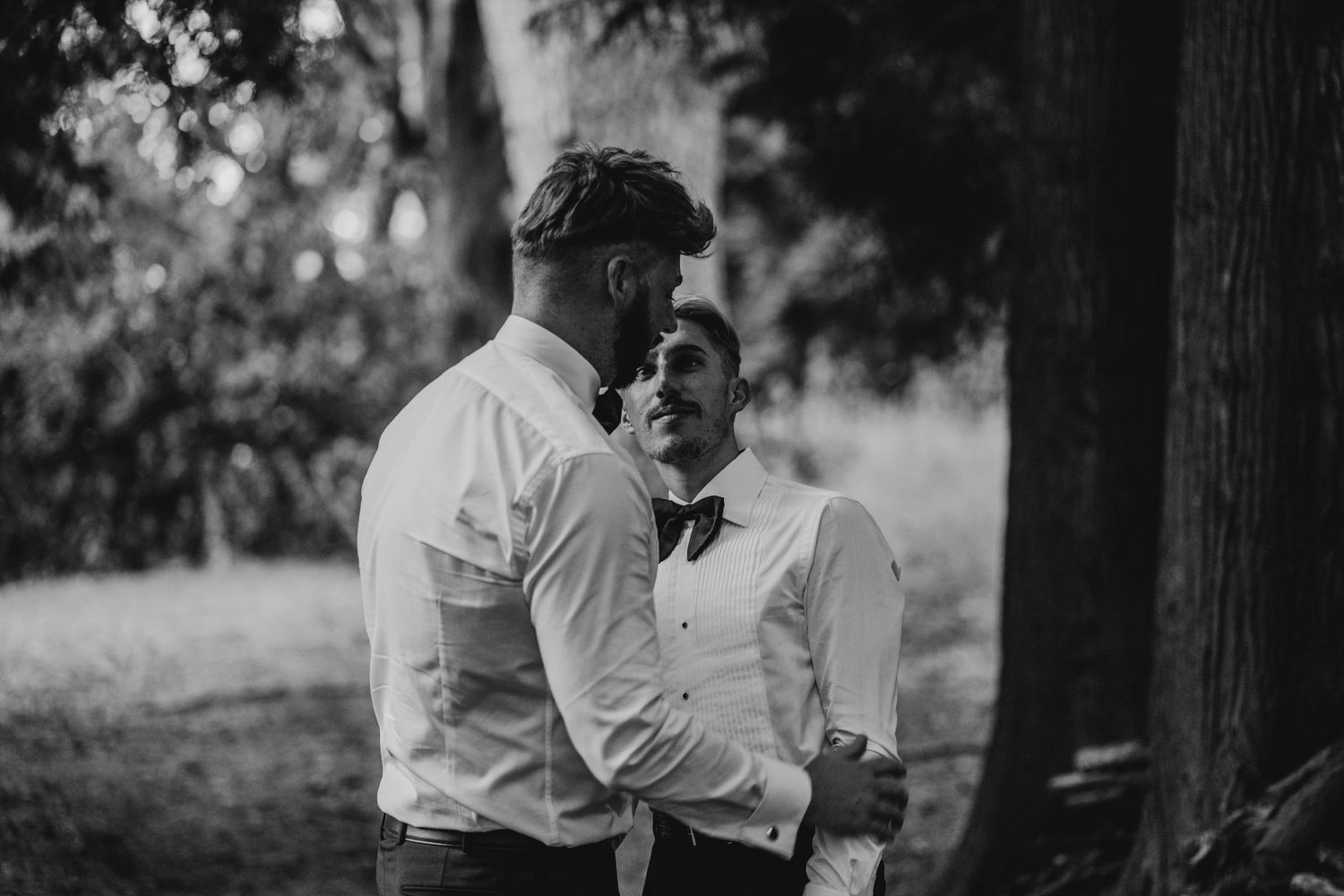 Two men in white shirts sharing a candid moment outdoors in black and white photography.