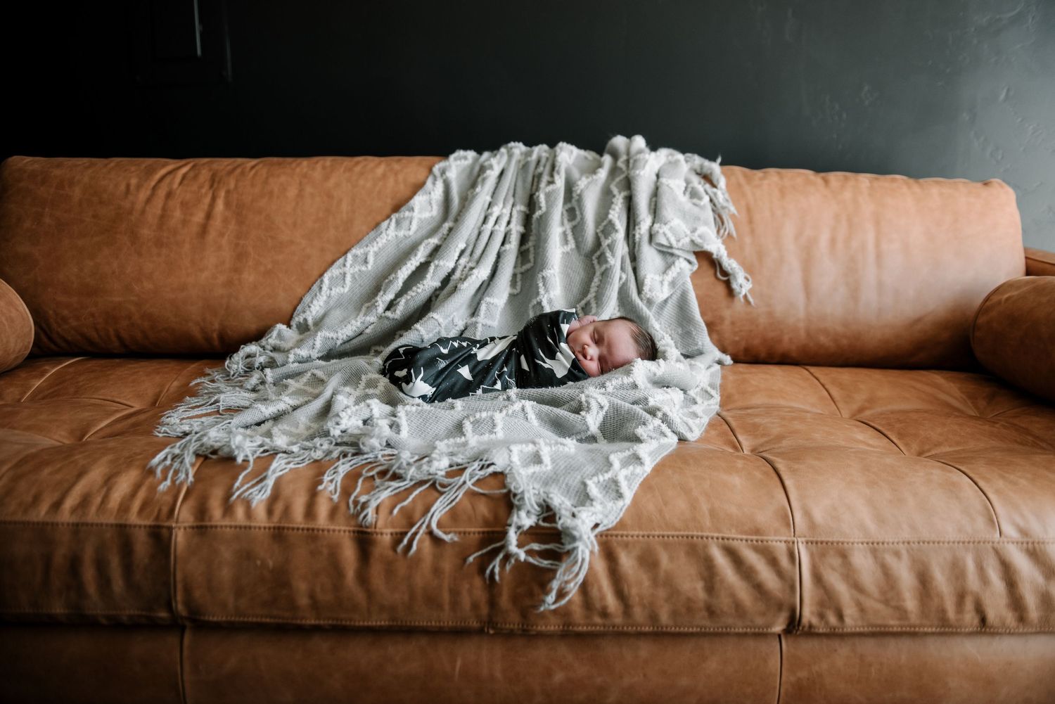 A soft gray blanket drapes over a brown leather couch in a minimalist setting.