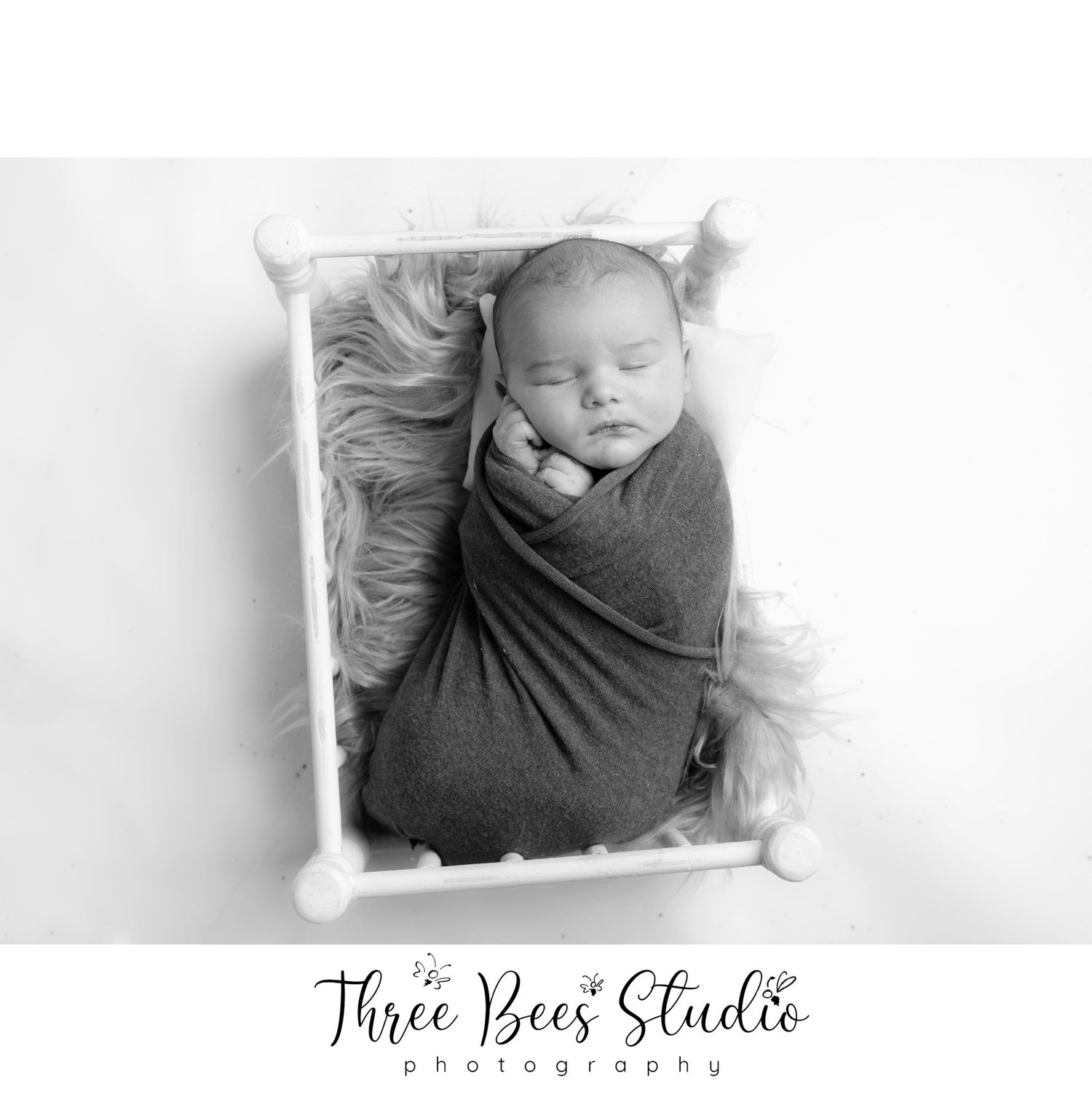 Black and white portrait of swaddled newborn sleeping in white frame.