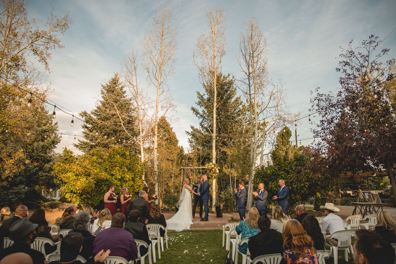 Outdoor autumn wedding ceremony with guests seated in garden setting.