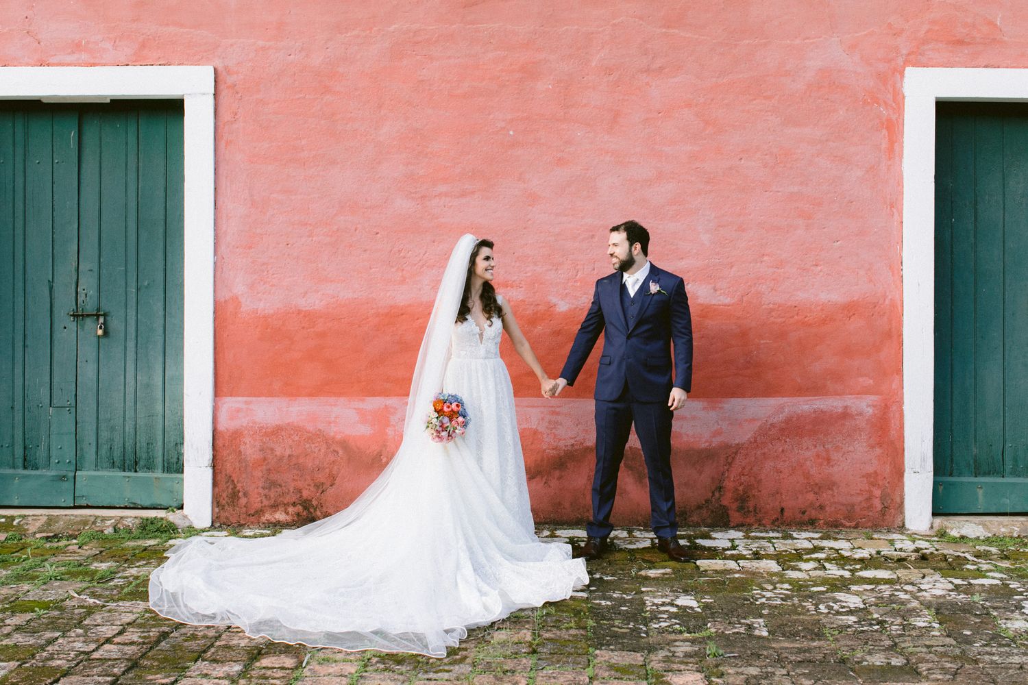 Elegant wedding couple posing in front of a coral-colored wall with green wooden doors.