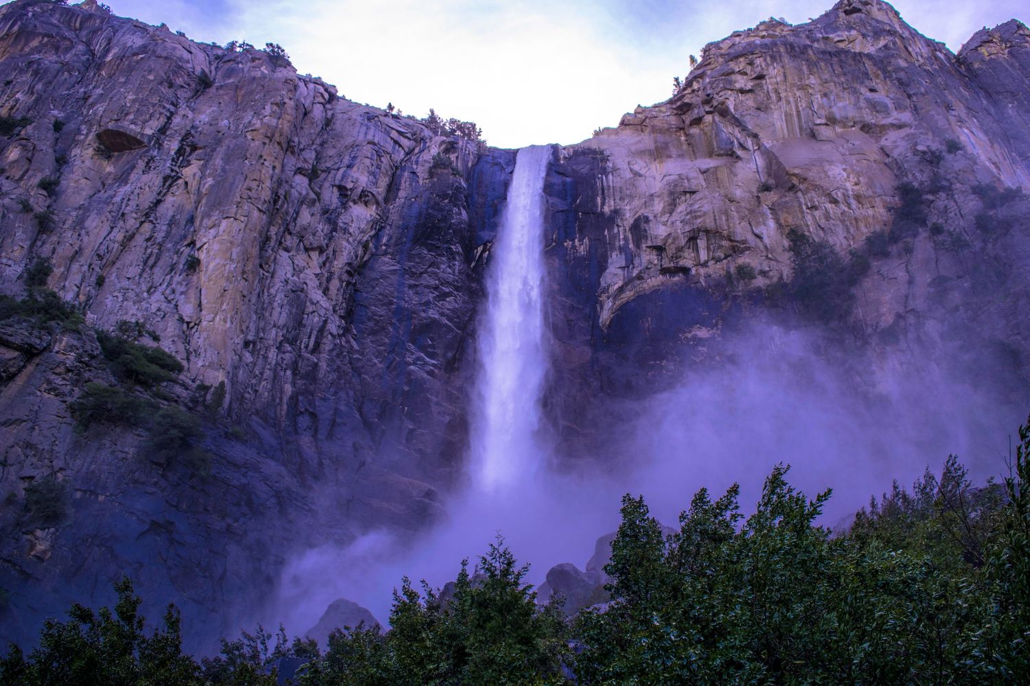Majestic waterfall cascades down steep granite cliffs in misty mountain landscape.