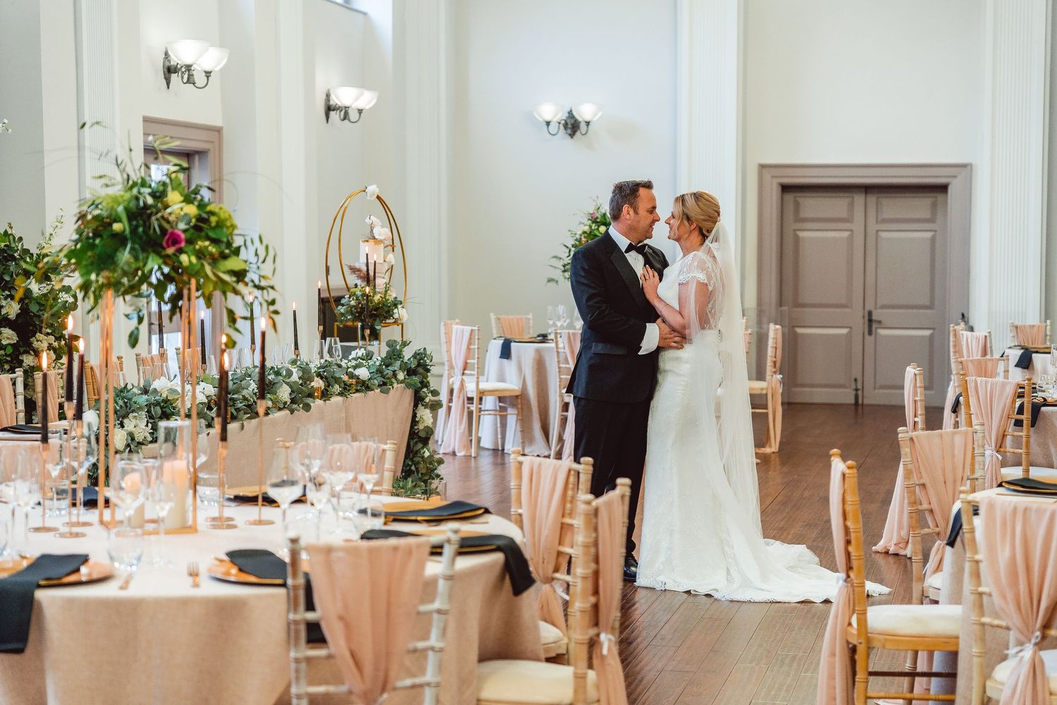 Elegant wedding reception venue with white chiavari chairs and floral centerpieces in a bright ballroom setting.