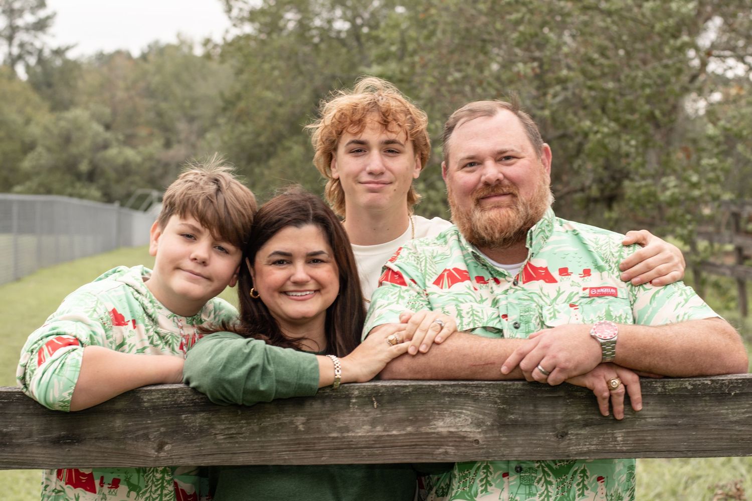 Family of four leaning on wooden fence wearing matching floral shirts outdoors.