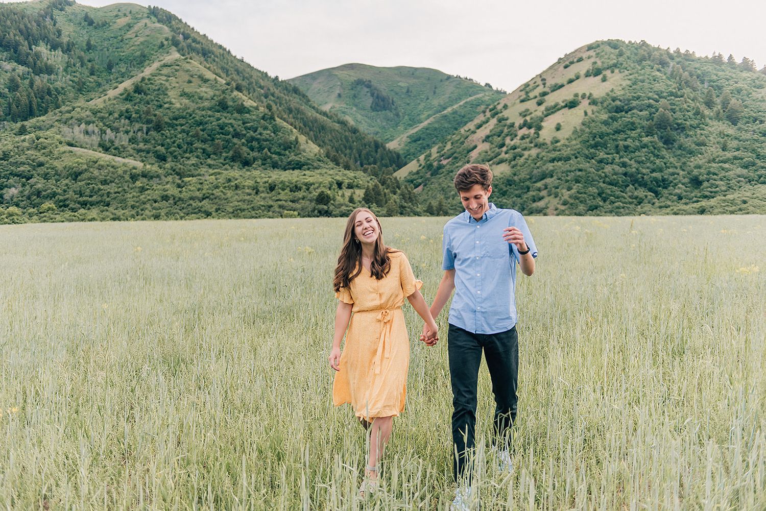 Couple holding hands while standing in mountain meadow with yellow dress and blue shirt.