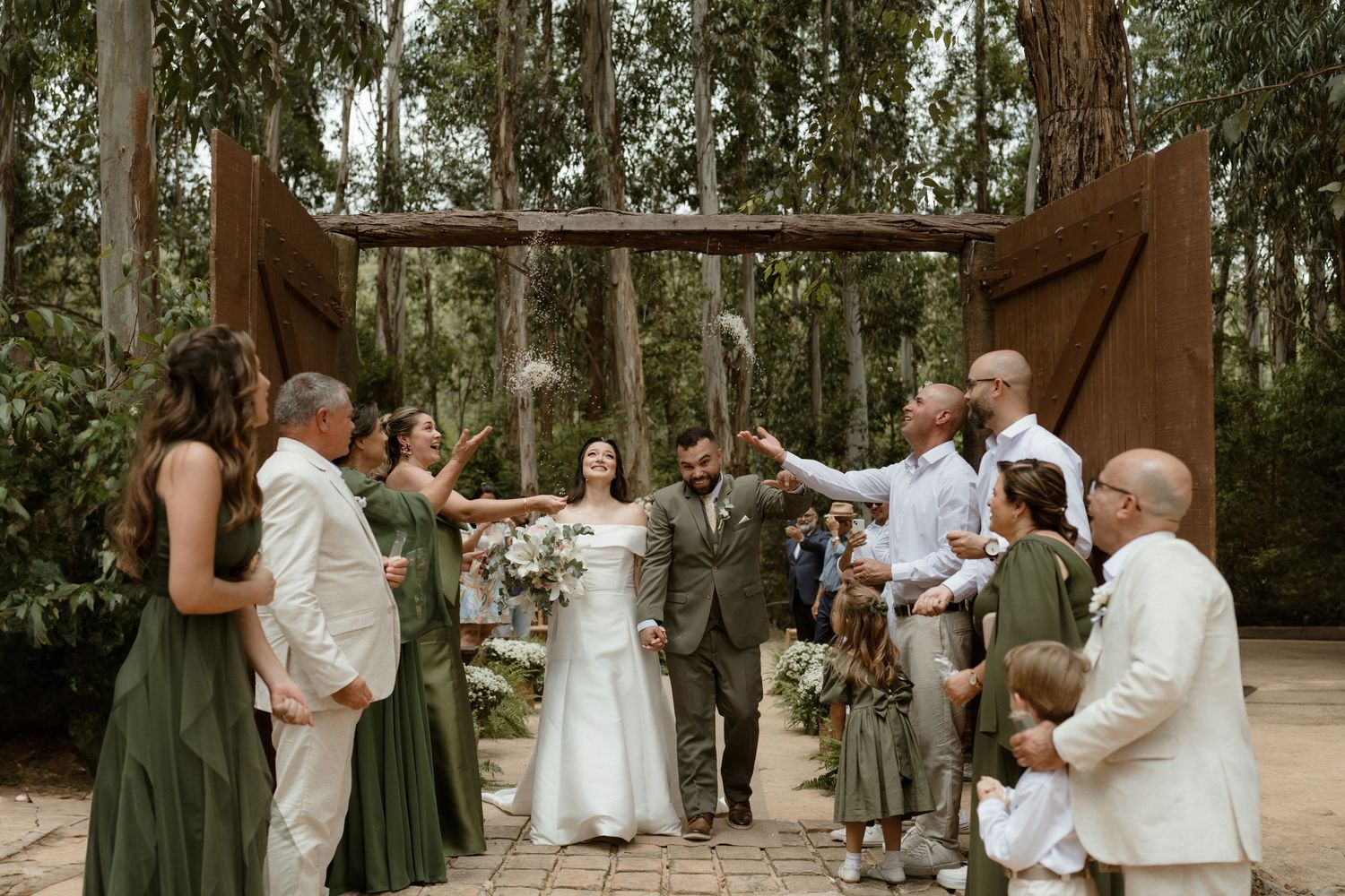 Wedding party members celebrate with joyful poses in an outdoor wooded setting.
