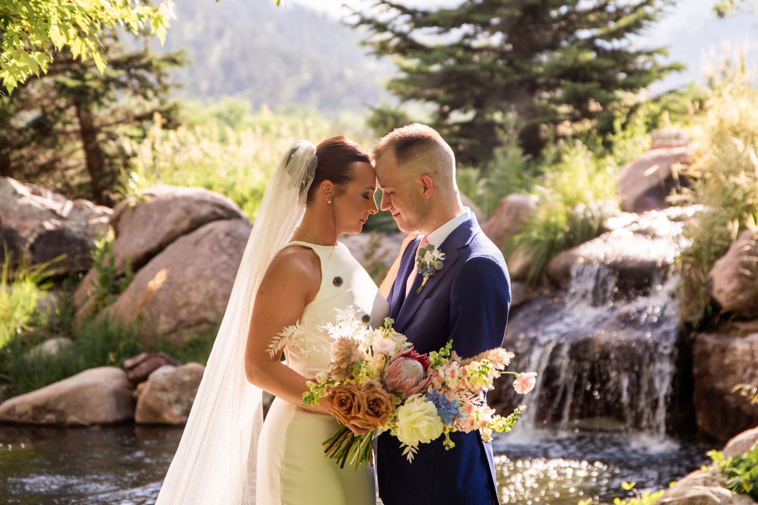Couple sharing intimate moment by waterfall in mountain wedding setting.