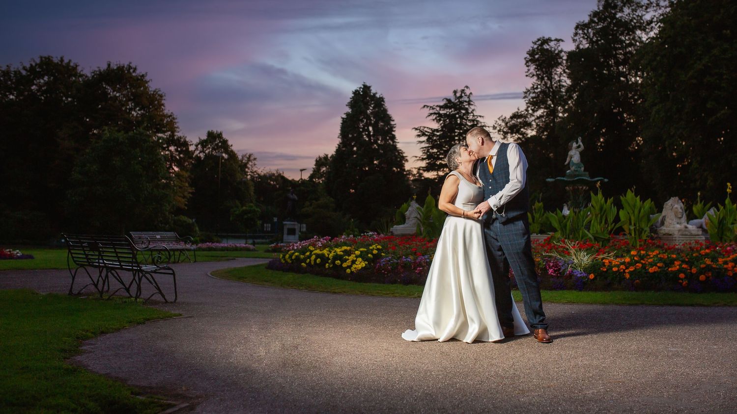 A romantic evening wedding portrait in a garden with colorful flowers and dramatic dusk lighting.