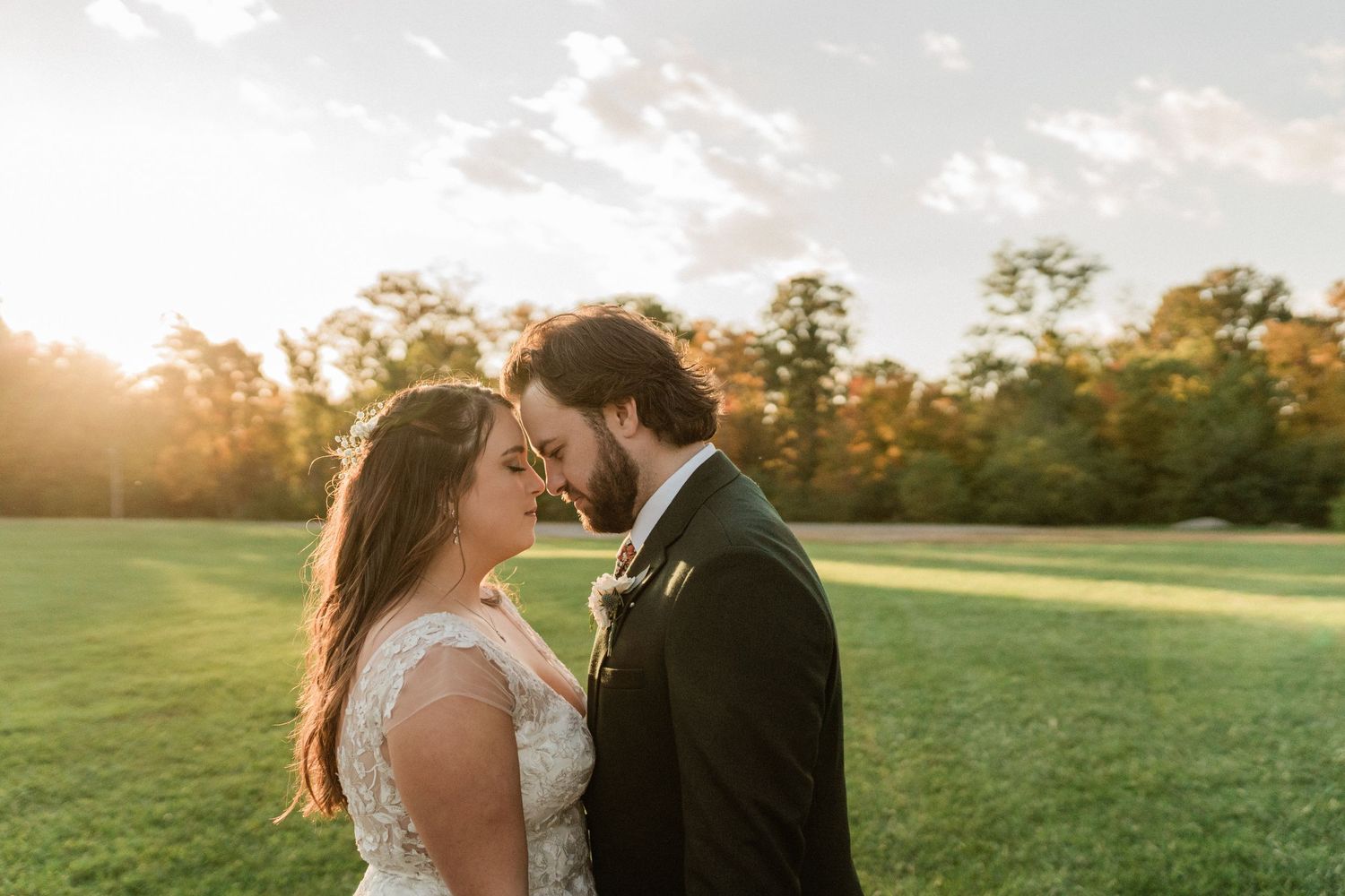 Newlywed couple sharing intimate moment during golden hour on grassy field.