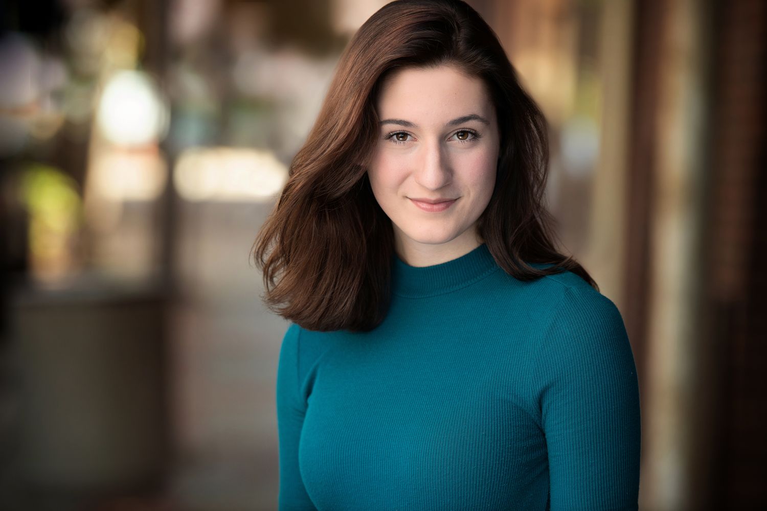 Studio portrait in teal sweater with warm lighting and architectural elements.