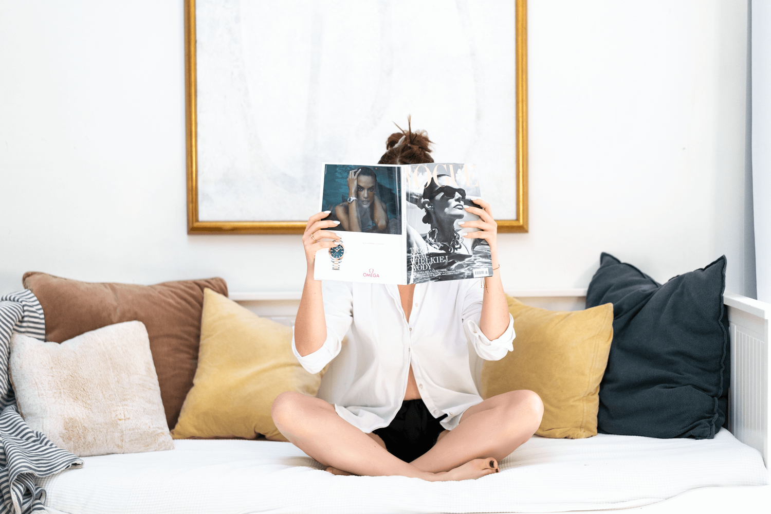 A relaxed reading session on a cozy bed with decorative pillows and a simple white frame.