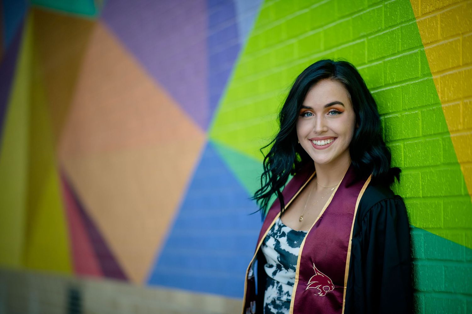 A person in a black cardigan smiles against a colorful geometric wall mural.