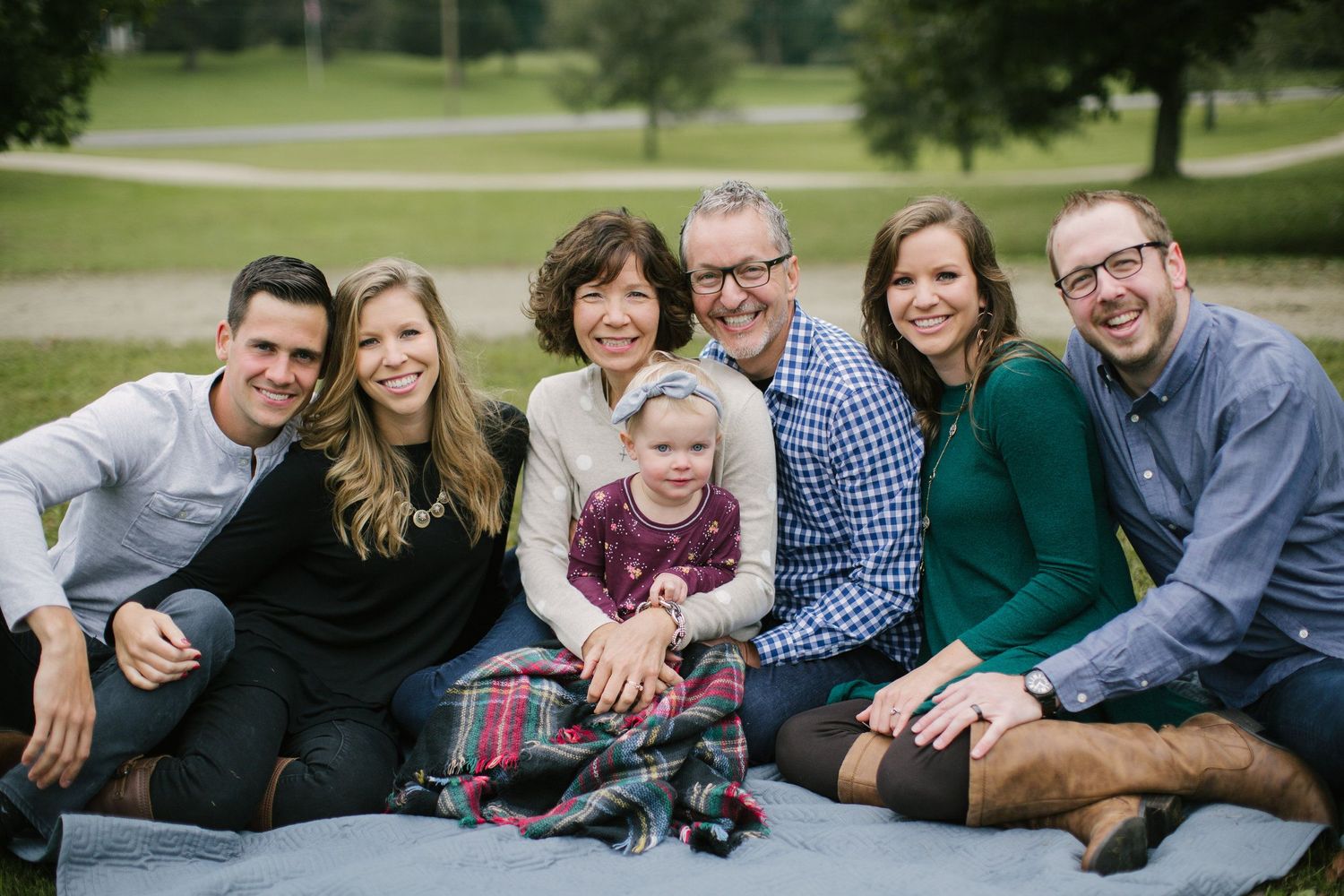 Family gathering outdoors on blanket in park for casual portrait session.