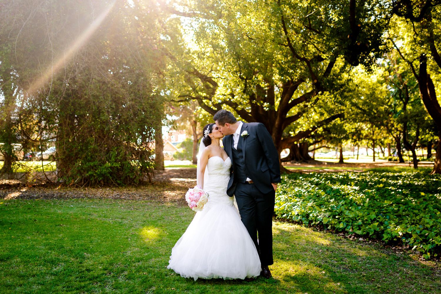 Newlyweds pose together under trees during autumn wedding photoshoot.