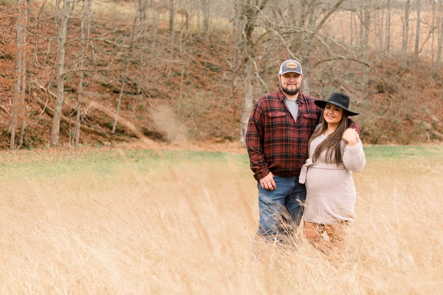 Couple poses together in a rustic autumn field with warm lighting.