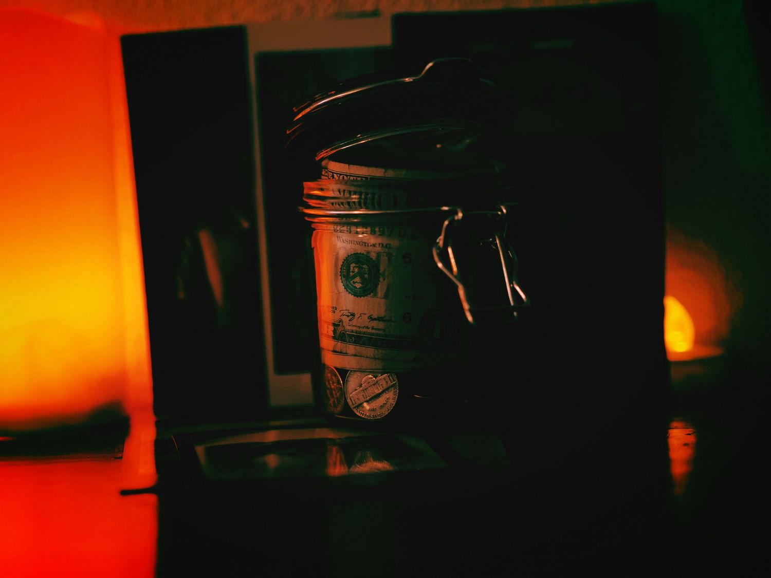 A jar of change and dollar bills sits on top of photographs and polaroids flanked by warm candlelight