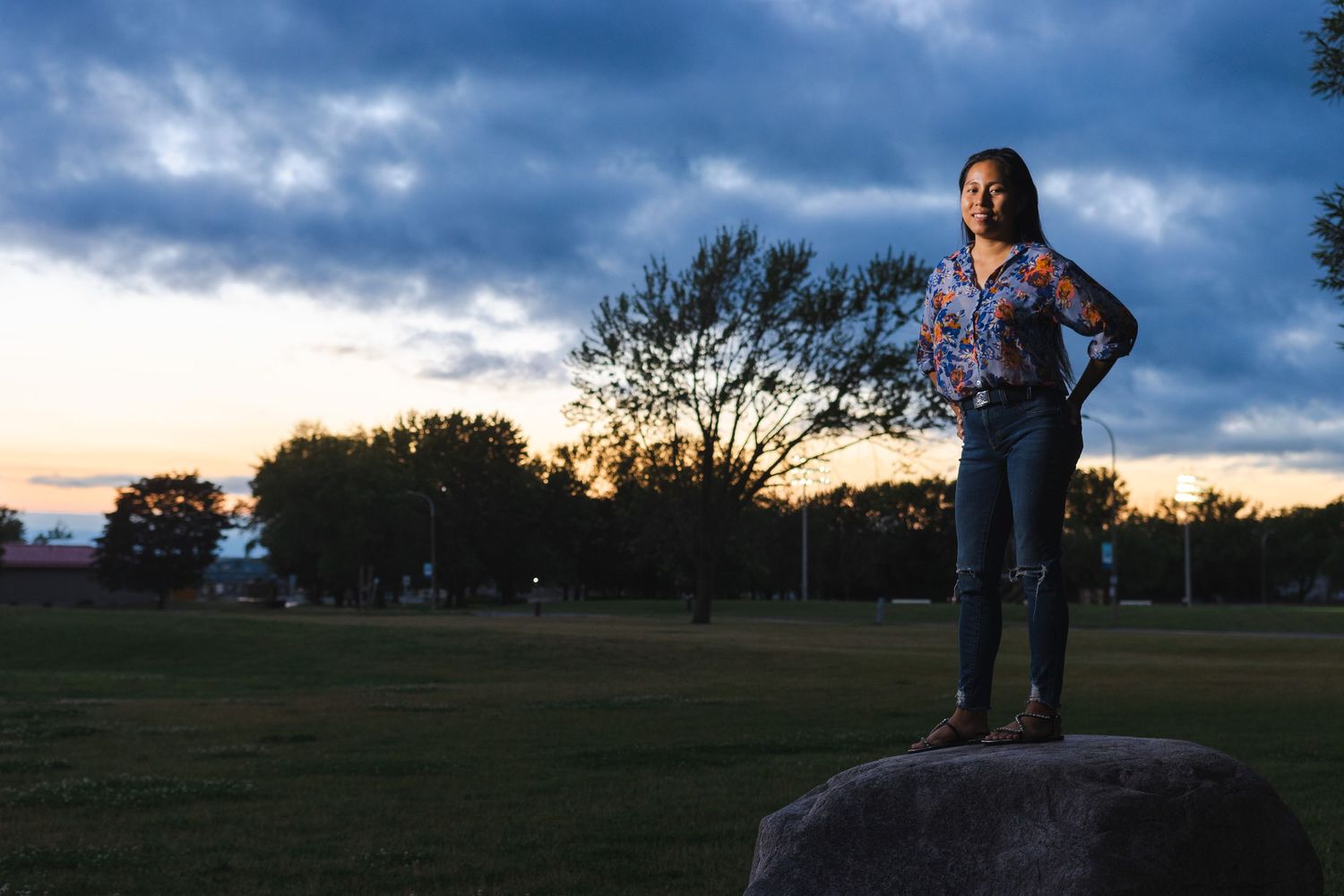 Silhouette of a person standing on a rock during sunset with dramatic cloudy sky in the background.