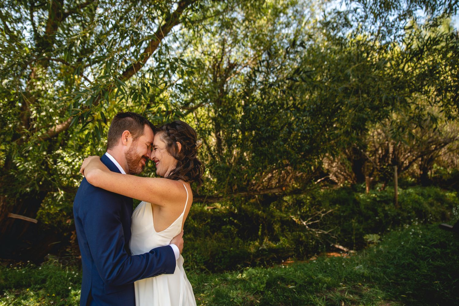 An intimate wedding embrace photographed against lush green foliage.