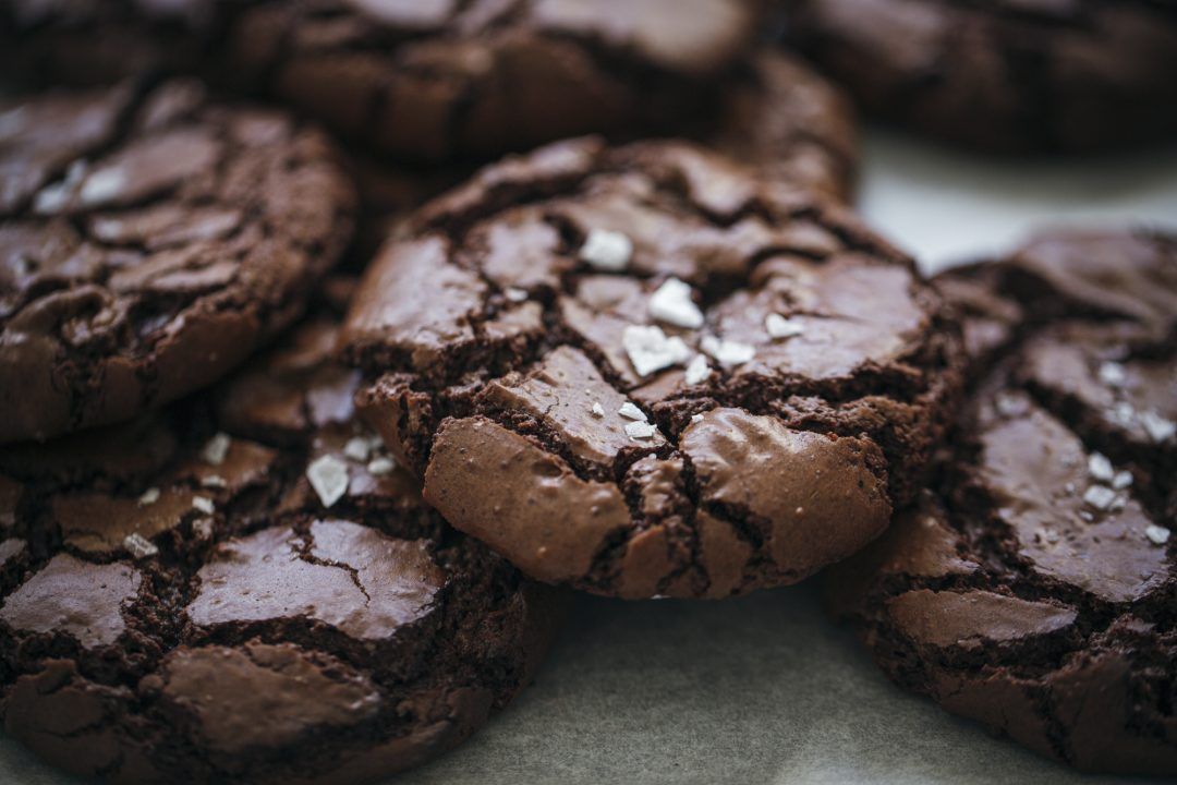 Chocolate crinkle cookies with crackled tops arranged on a dark surface.