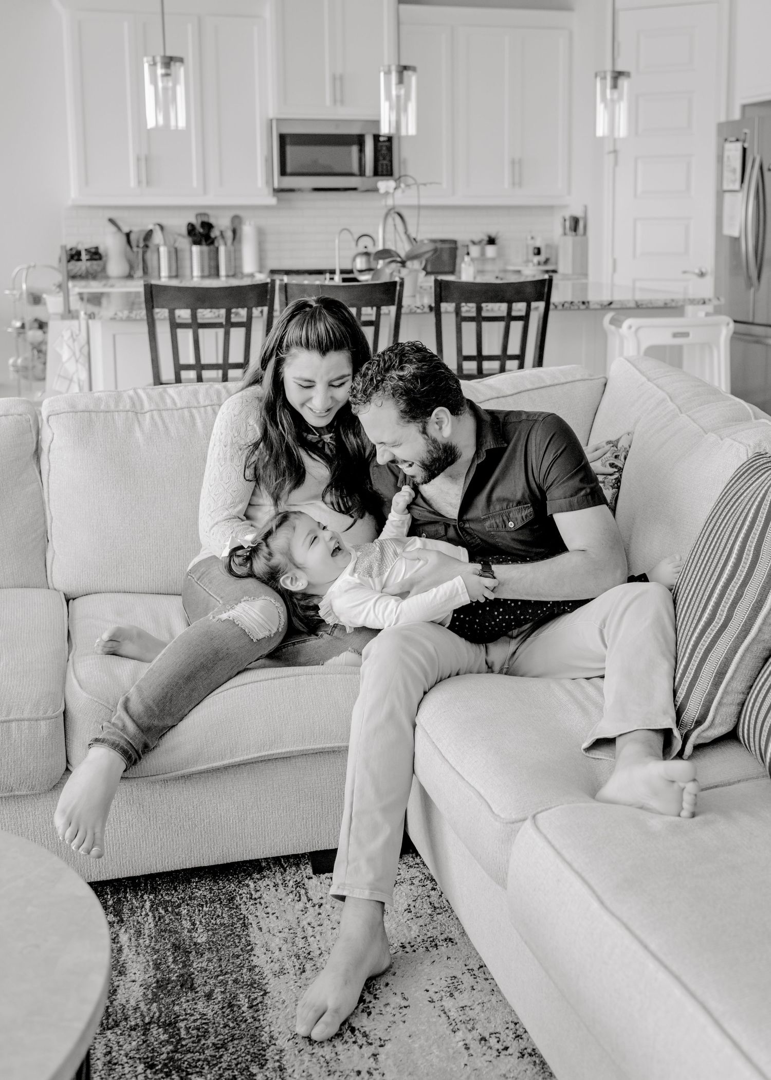 family sitting together on their couch. parents tickling their daughter as she giggles