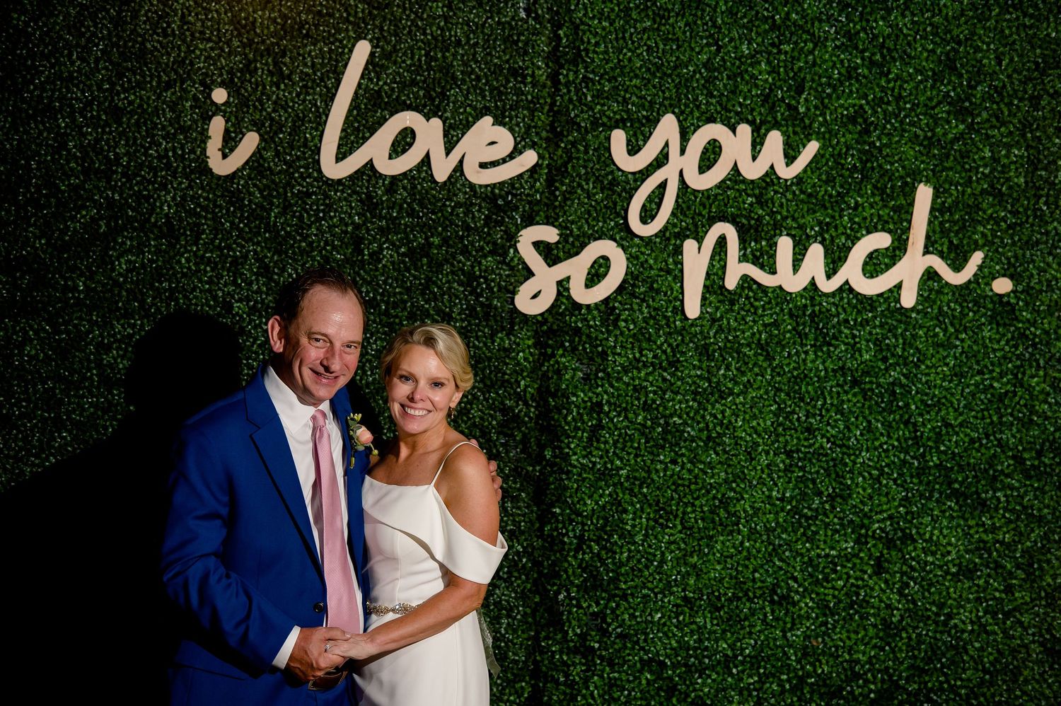 Wedding couple posing against green wall with 'i love you so much' text display.