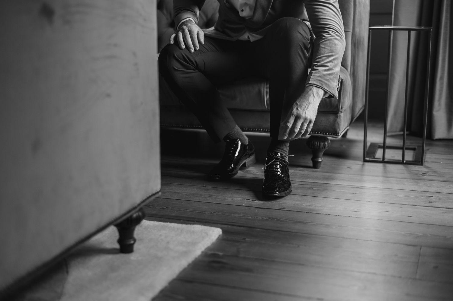 Close-up black and white photo of someone adjusting dress shoes while sitting.