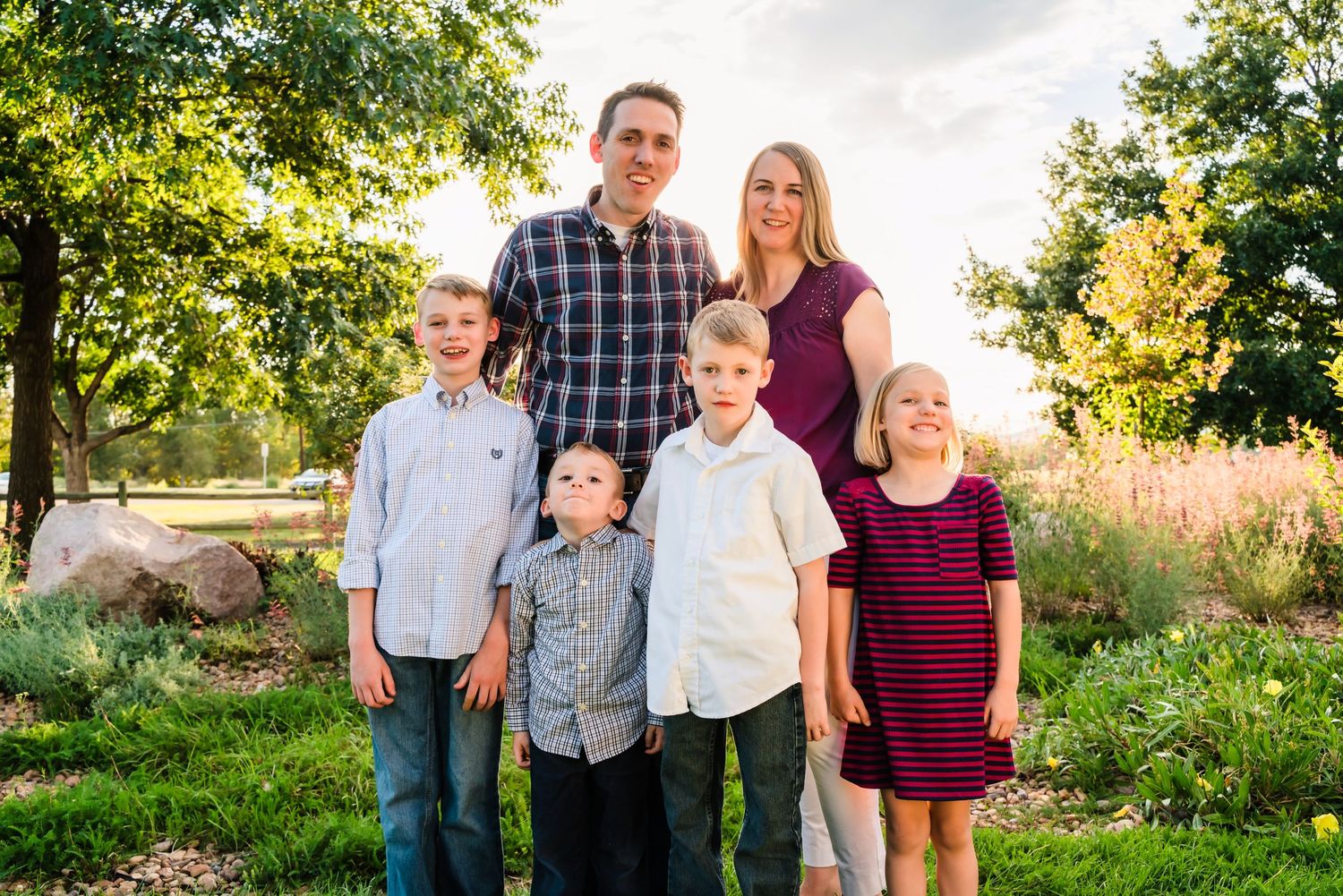 Family of five standing together outdoors in coordinated outfits during golden hour.
