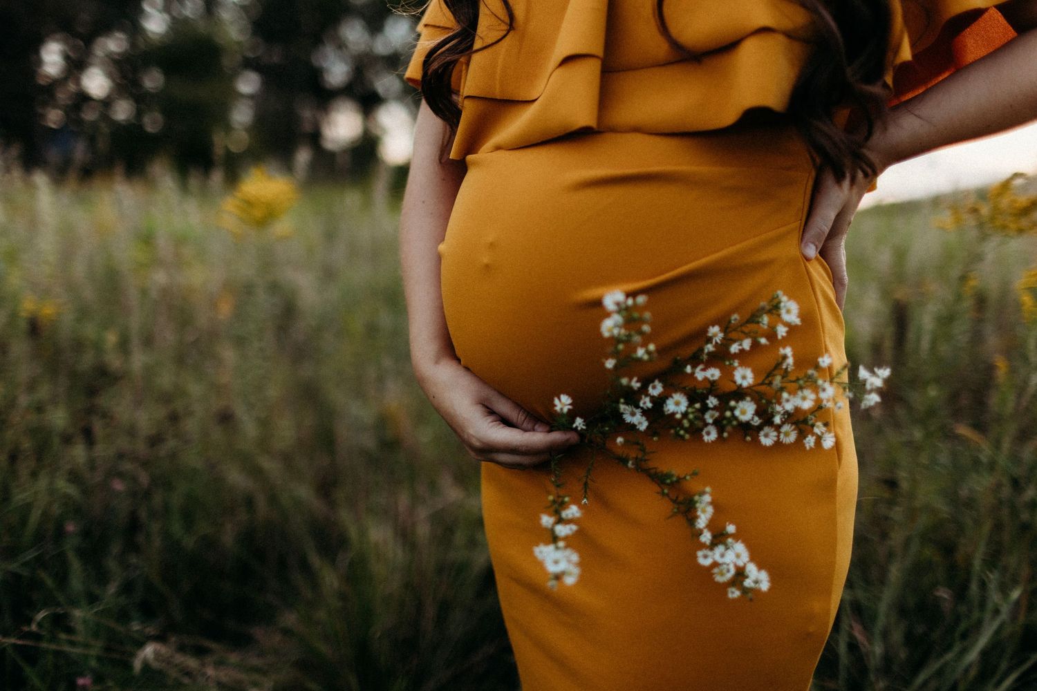 Close-up of yellow maternity dress with small white flowers in natural outdoor setting.