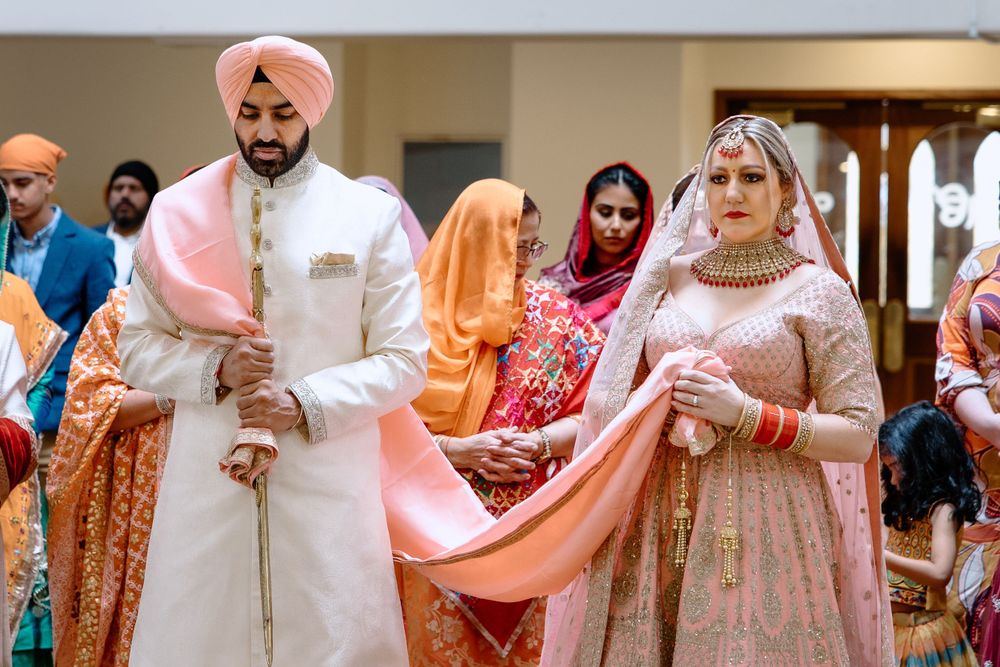 Traditional Sikh couple in elegant pink and cream wedding attire during their cultural ceremony.