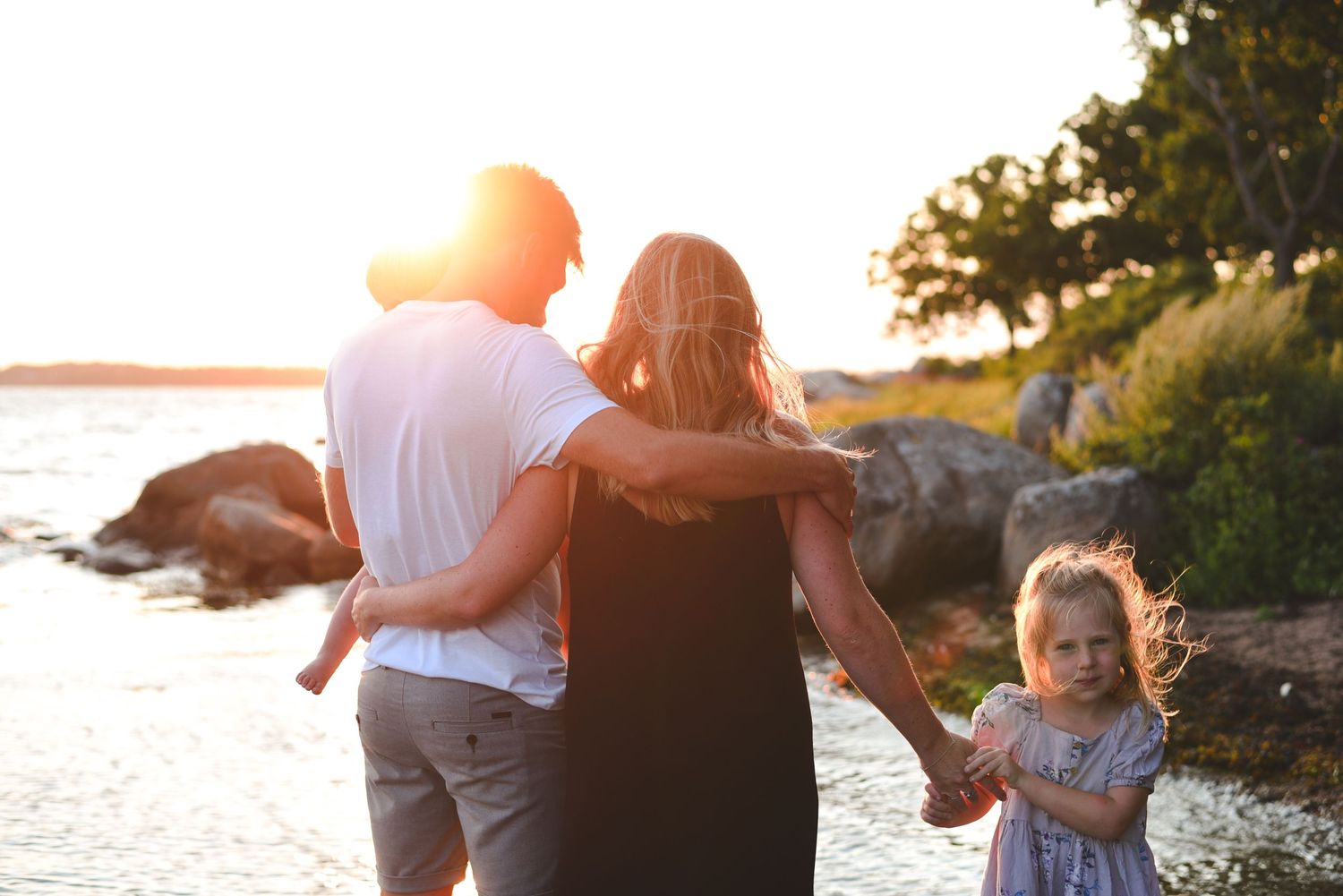 A family enjoying a sunset walk together along a rocky beach shoreline.
