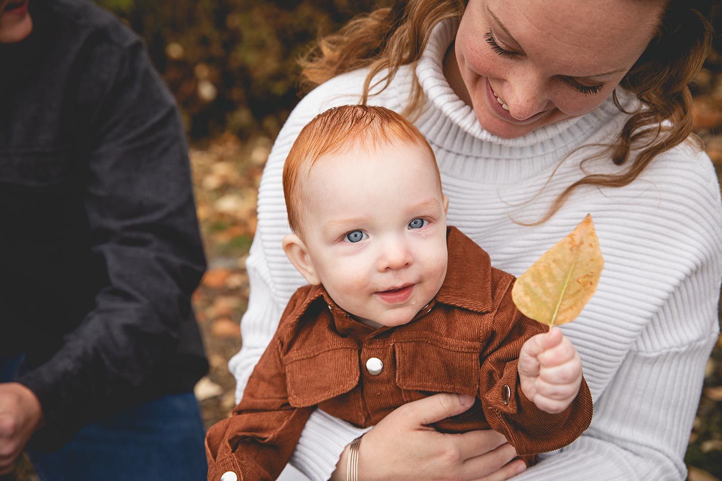 baby sitting on mom's lap and holding a leaf in the fall