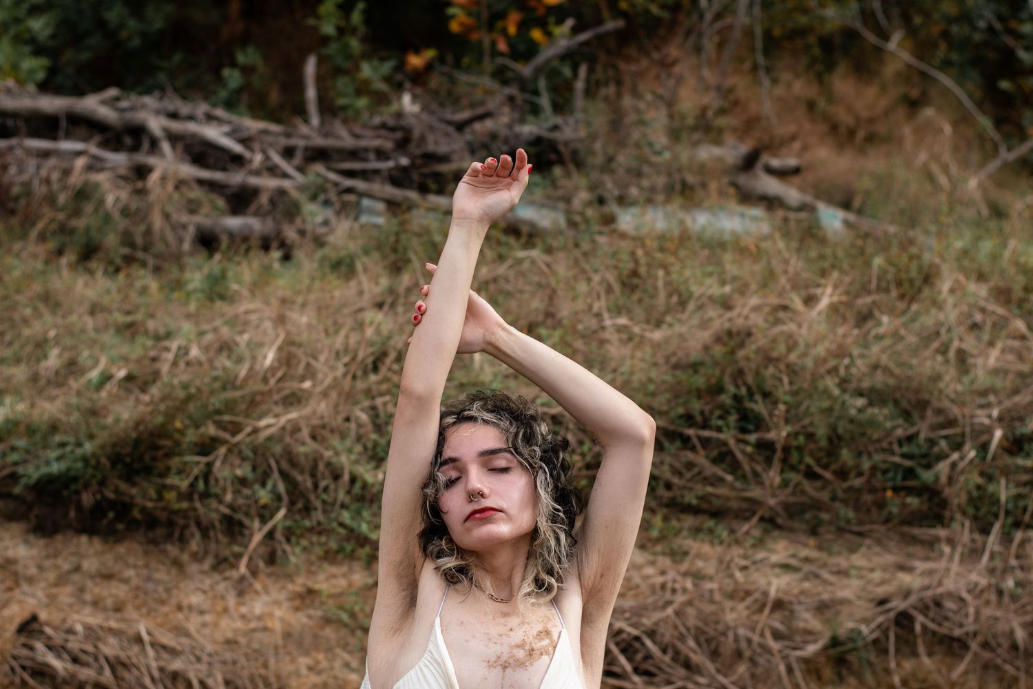 A dreamy artistic portrait of someone posing with raised arms in a natural outdoor setting.