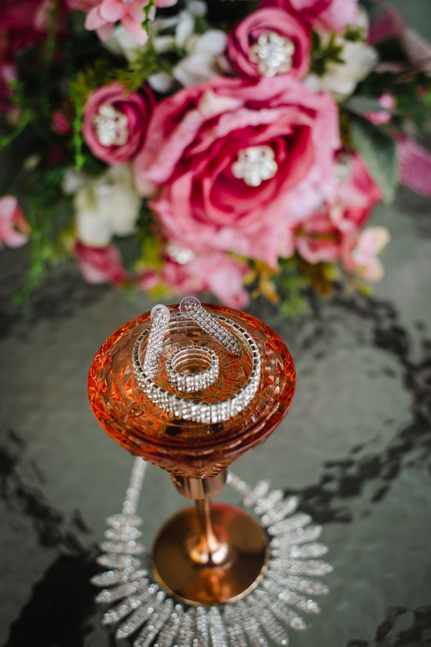 Flatlay of perfume bottle, earrings, ring, wedding dress, and bouquets in the background